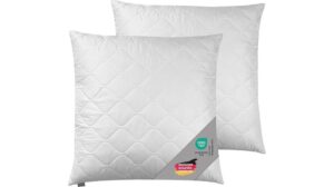 Zwei weiße Traumnacht-Kuschelkissen mit sichtbaren Nähten und Etiketten, die für optimalen Komfort übereinander liegen.