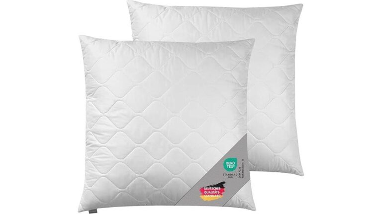 Zwei weiße Traumnacht-Kuschelkissen mit sichtbaren Nähten und Etiketten, die für optimalen Komfort übereinander liegen.