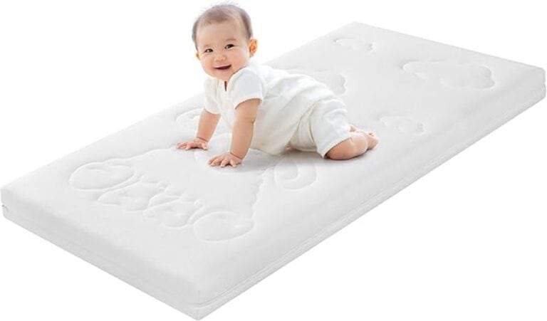 Ein Baby in Weiß krabbelt auf einer Traumnacht-Babymatratze mit Wolkenmuster, schaut nach oben und lächelt.